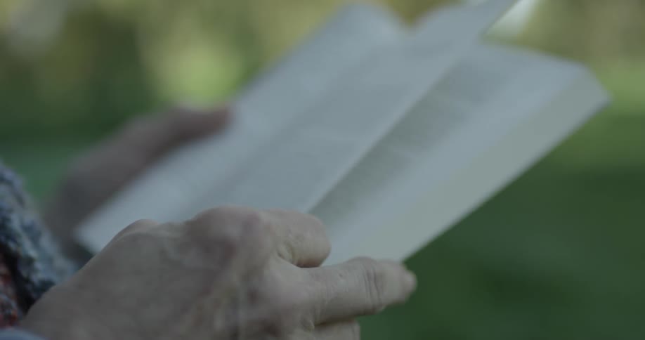 An elderly person is reading a book and turns to the next page