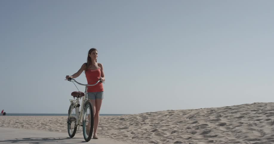 Woman walking a bike down a path at the beach