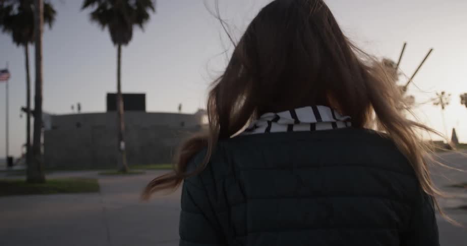 A woman turns and walks backwards on a path in the setting sun