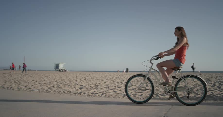 Woman rides a bike on a sidewalk next to the beach
