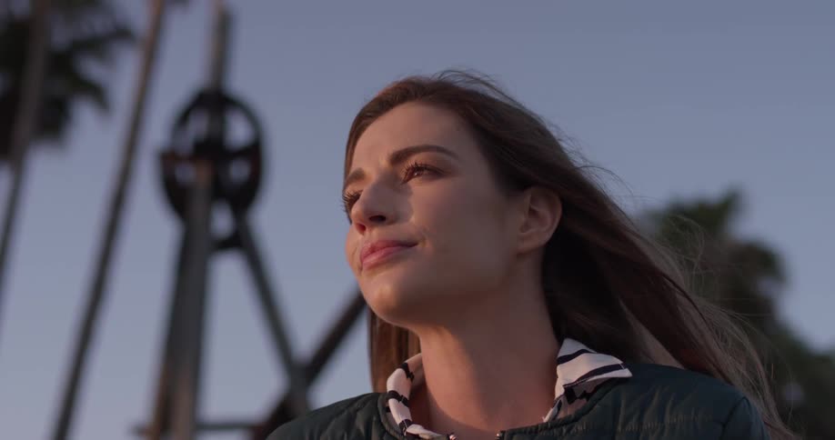 Beautiful women in a puffy jacket stares off at the sunset on a blue sky day