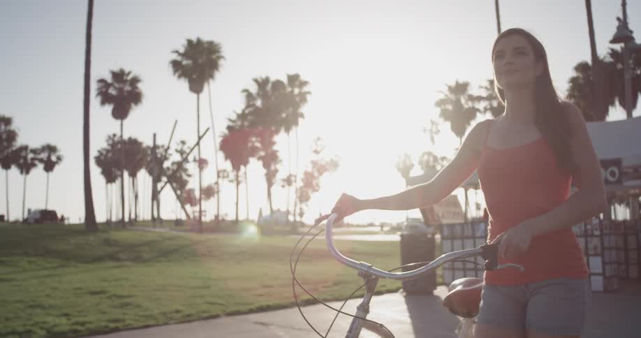 A woman walks her bike along a path as the sun shines brilliantly in the background