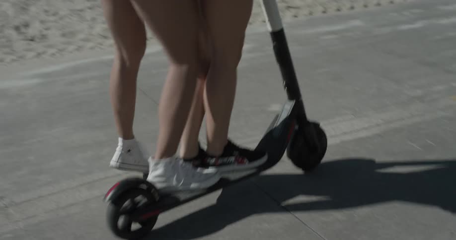Two women ride on a small scooter by the beach