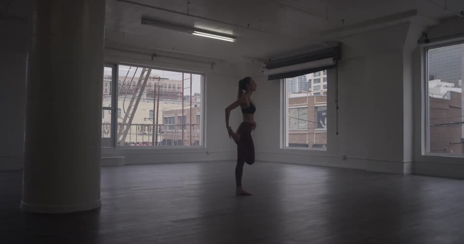 A woman stretches her leg as she stands on a wooden floor