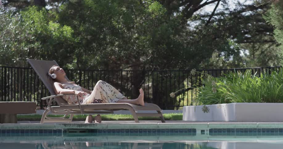 A woman puts on headphones sitting beside a pool