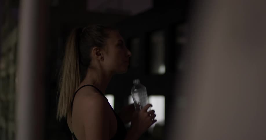 A woman takes a drink from a water bottle in a large dark room