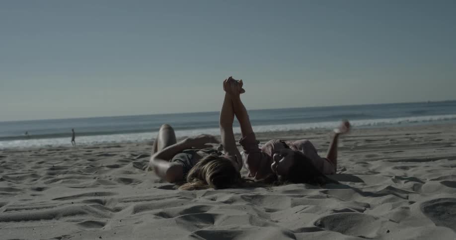 Two people hold hands and raise them while laying on the beach during the day