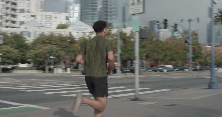 A man jogging down city streets with palm trees and tall buildings in the background