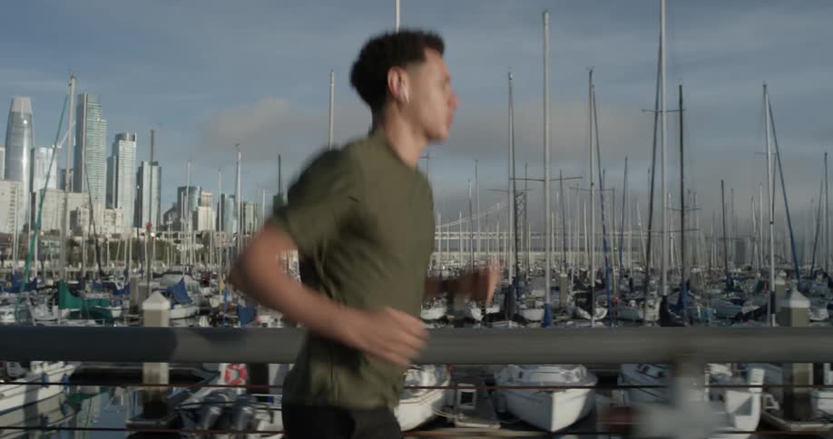Man with short hair is jogging by a boat park filled with tons of boats on a cloudy sunny day