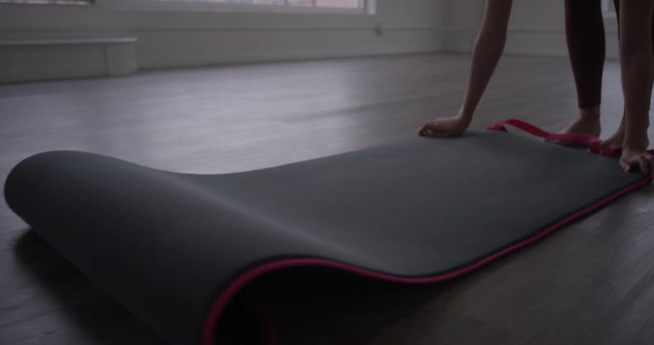 A woman puts a yoga mat on the floor and straightens it out