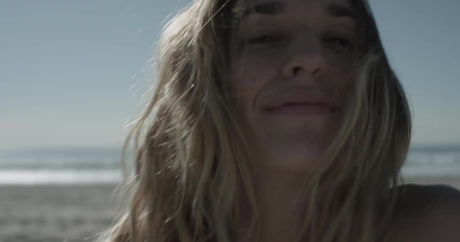 Woman on beach playfully sprinkling sand and touching her hair