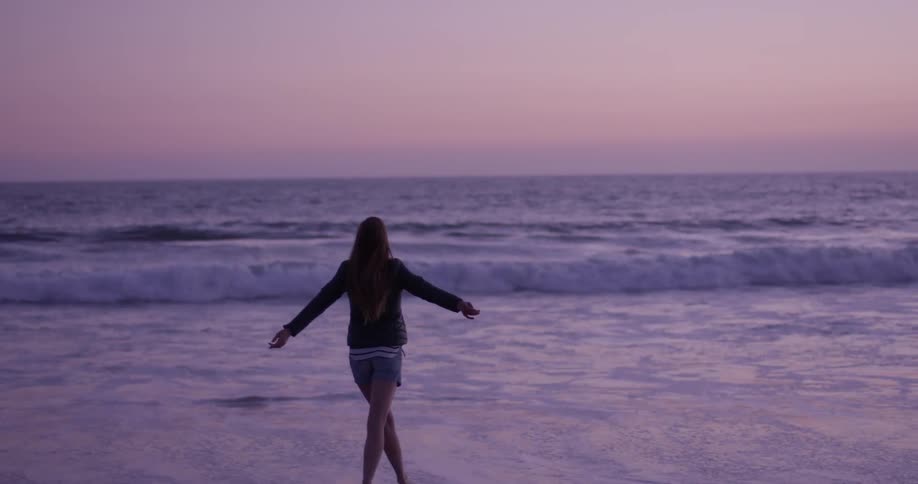 A woman runs up to the water edge and prances in the ocean