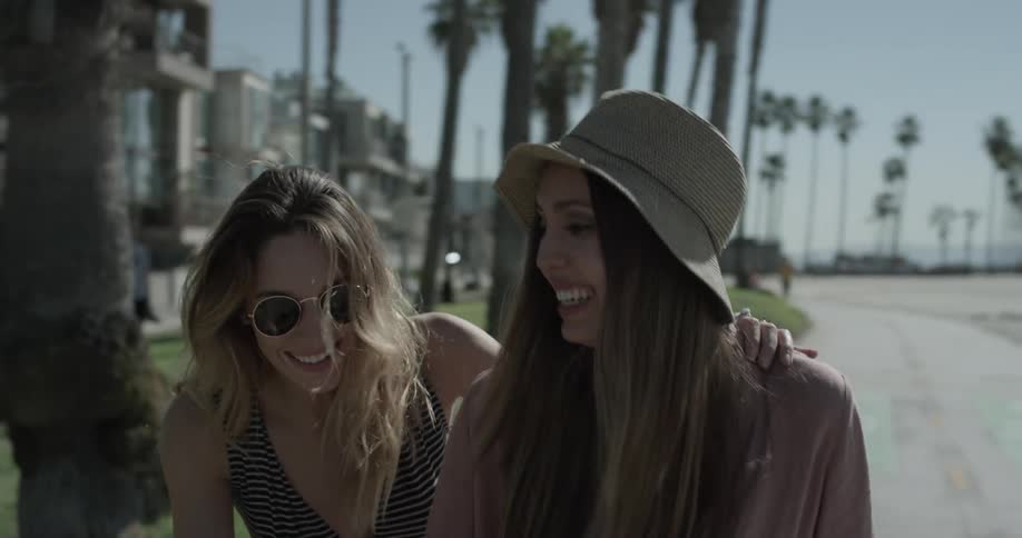 Two woman laughing as they attempt to ride a scooter together