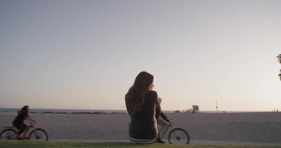 Two bikers ride passed a woman sitting in the grass