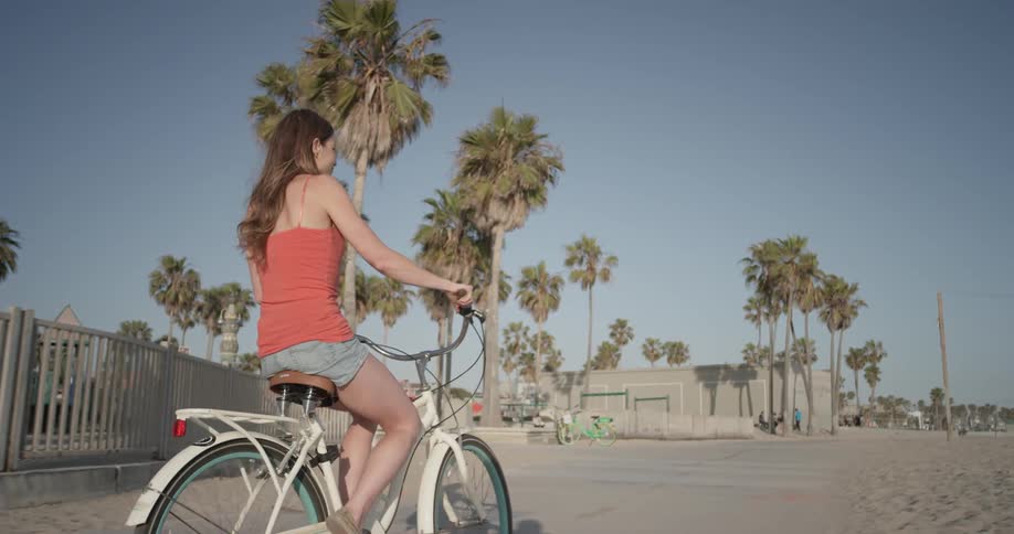 A woman rides her bike past a fenced in playground