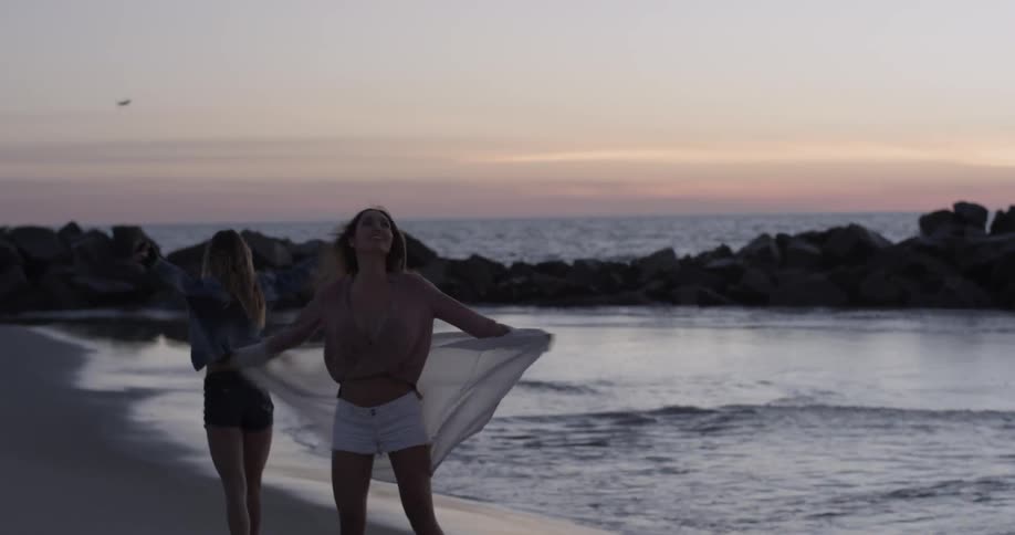 Two women twirl around on beach near the water