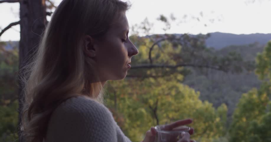 A woman sips from a mug of tea then closes her eyes contentedly