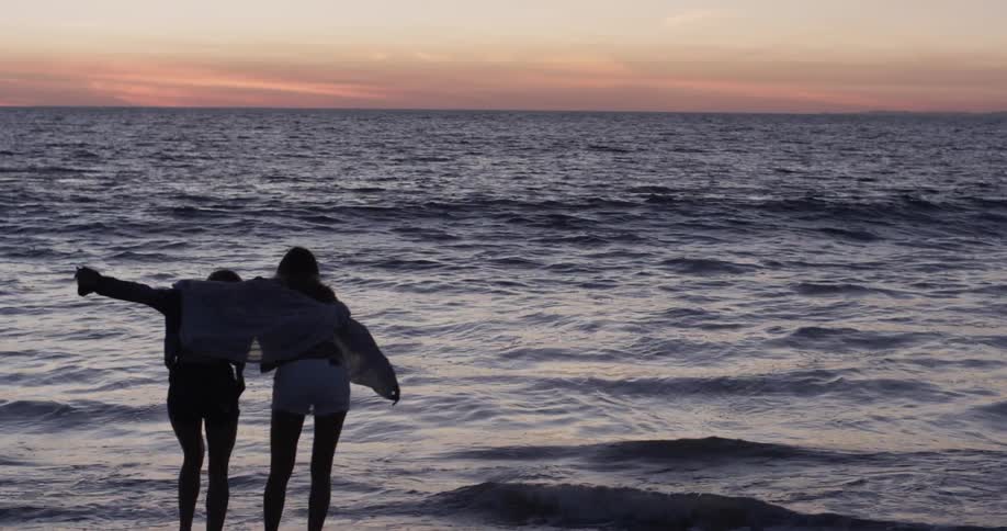Two women running towards the ocean and hugging