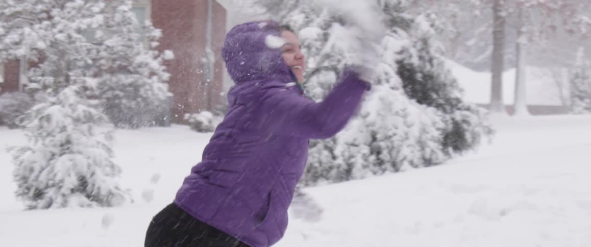 A girl in a winter coat throws a snowball on a snowy day