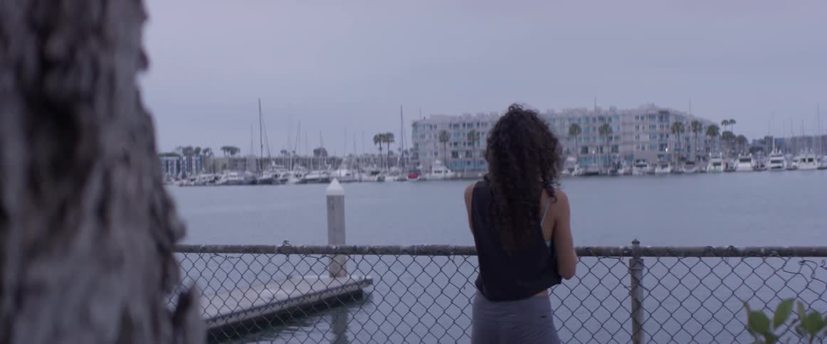 A woman stands by a fence with her cell phone