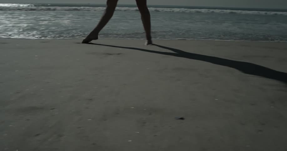 An energetic women is doing cartwheels on the beach near the water and dodging waves as they come in on a very sunny day