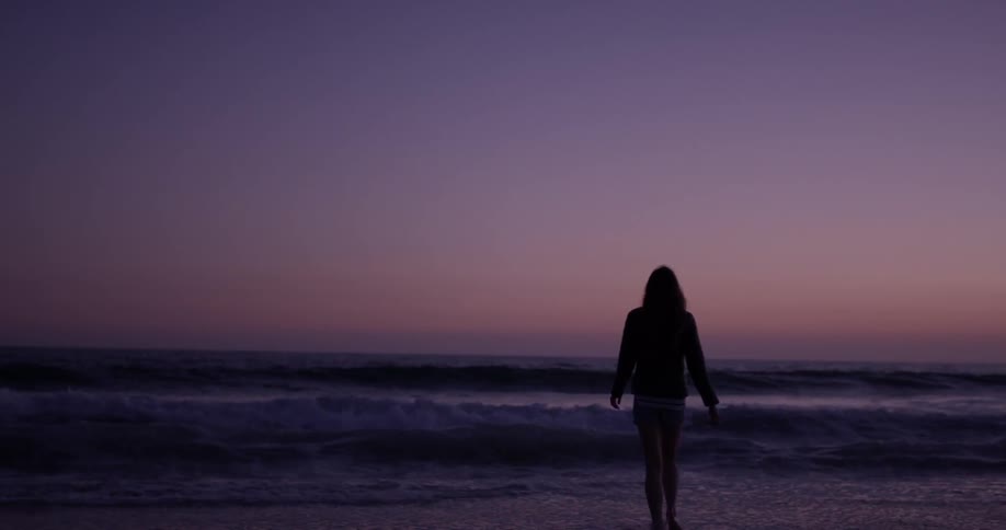 Woman walks on the beach at sunset