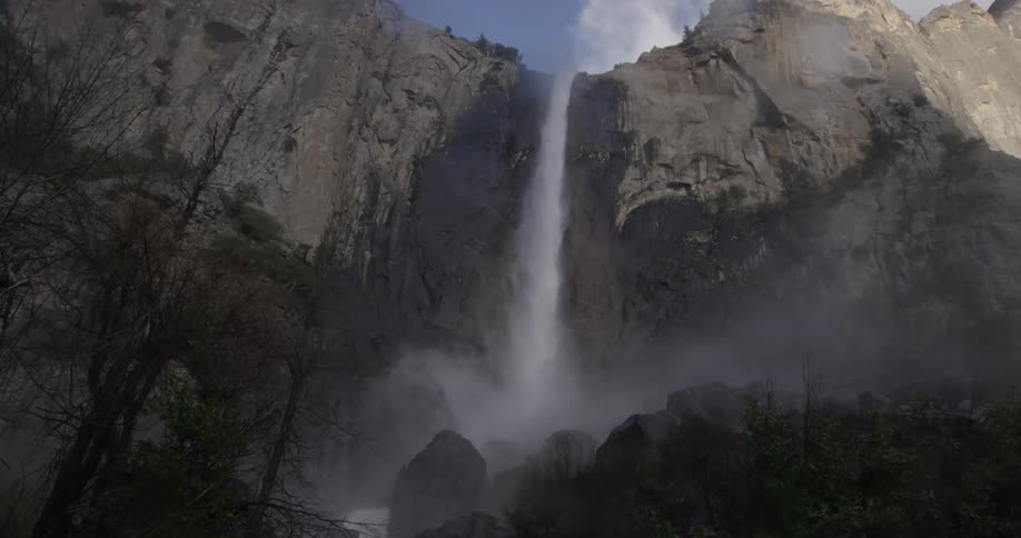 Water falls off a waterfall into the valley below full of rocks creating mist for the trees and plants
