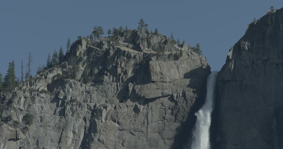 A very tall waterfall between two tree lined mountains