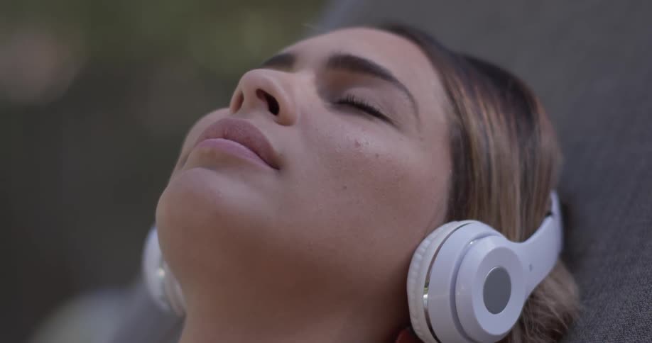 A woman is laying down and puts on headphones