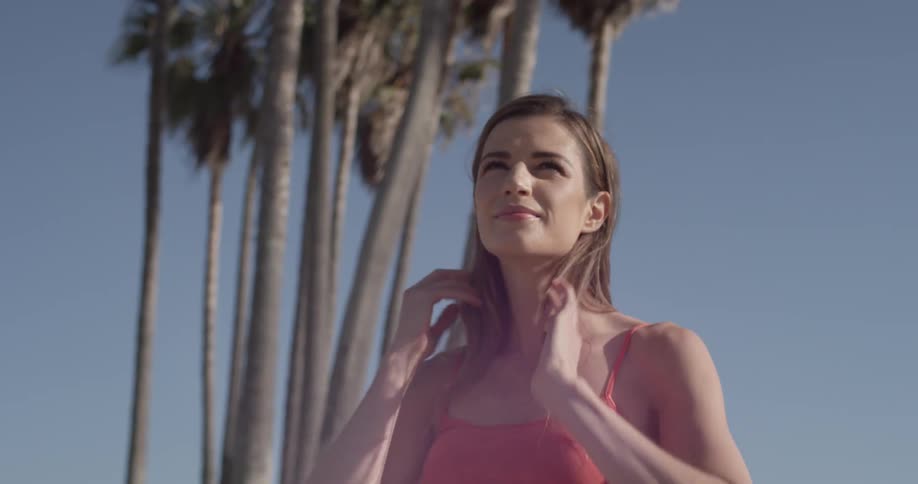 Woman smooths her hair back while standing outside on a sunny day