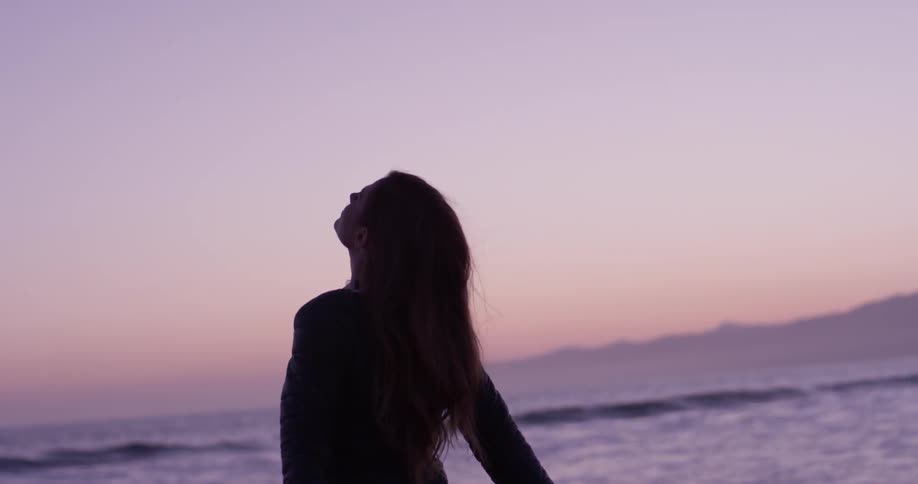 Woman looking up at the sky at sunset next to the ocean