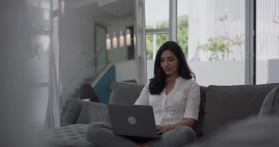 Woman sits on a couch typing on a laptop