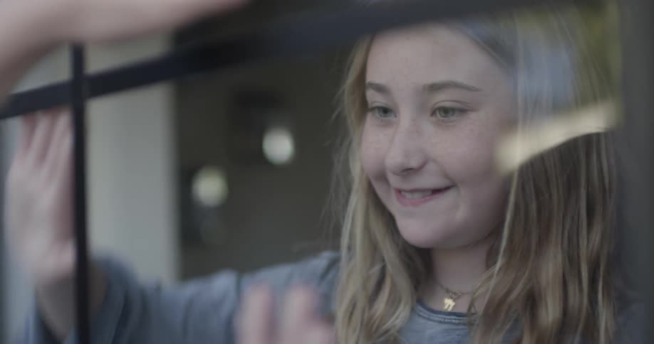 Two children play patty-cake through a window pane