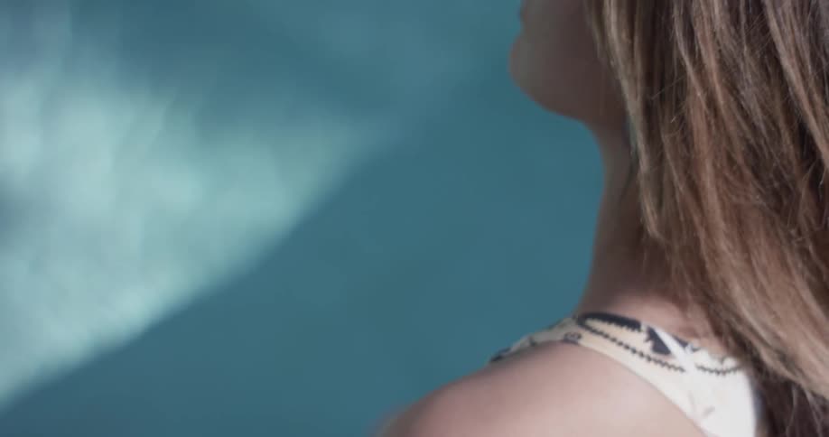 Closeup of  a shoulder and head of a woman sitting poolside and playing with her hair