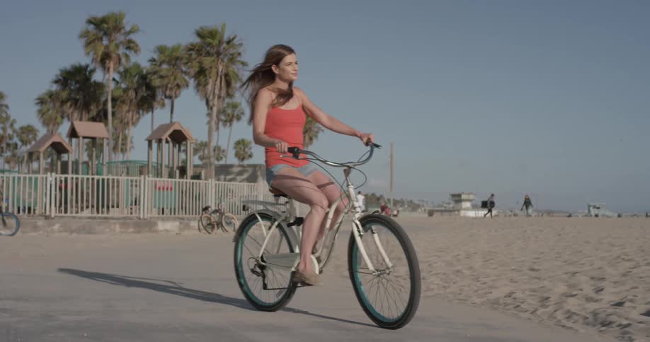 A beautiful women rides her bike down the sidewalk at the beach on a beautiful sunny day