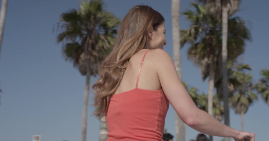 Woman rides a bike past palm trees on a sidewalk