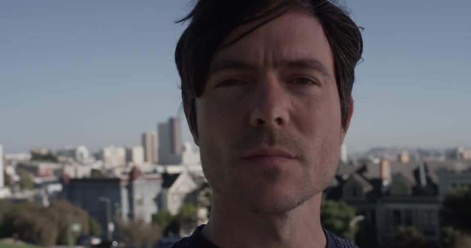 Man stands looking out with a city behind him
