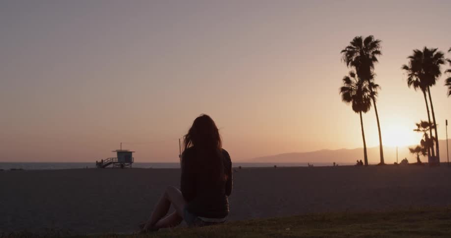 Woman sits on the beach at sunset