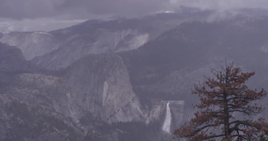 Clouds cover a mountain as a waterfall rushes from the middle of it