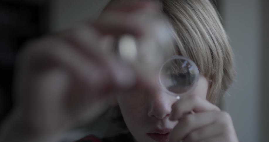 A boy looks at something in his hand with a magnifying glass