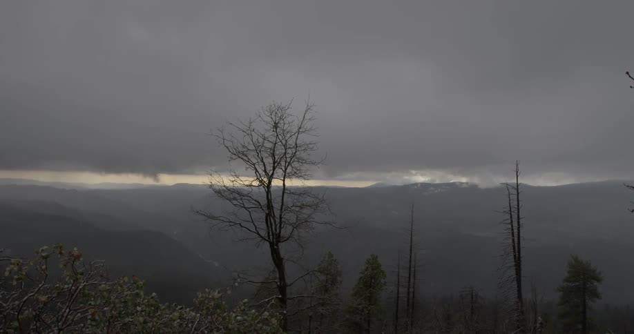 Rain falls over a mountain range landscape with rainy clouds above and dimly lit skies