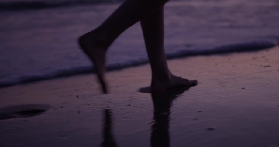 Closeup of a woman's feet walking through the ocean surf at dusk