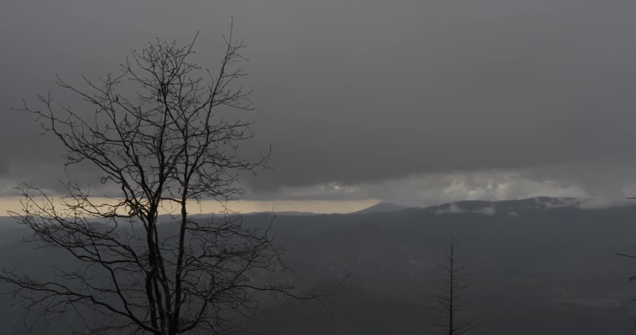 Camera looks out at a nature landscape of mountains and cloudy skies on a dark day outside