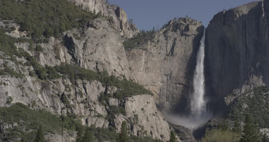 Water falls off a cliff into the valley below creating mist and water droplets for the plants and trees there