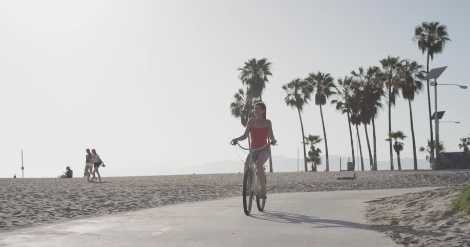 Woman rides a bike down the sidewalk next to a sandy beach