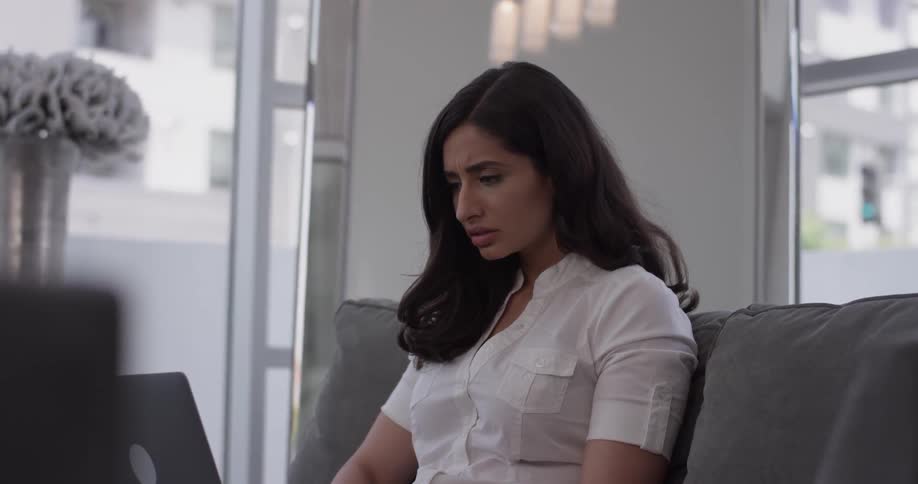 A woman looking shocked at something she's reading on a laptop
