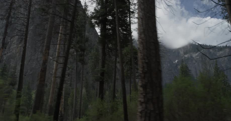 Trees move past as we see a huge cliff in the background with fluffy clouds over them