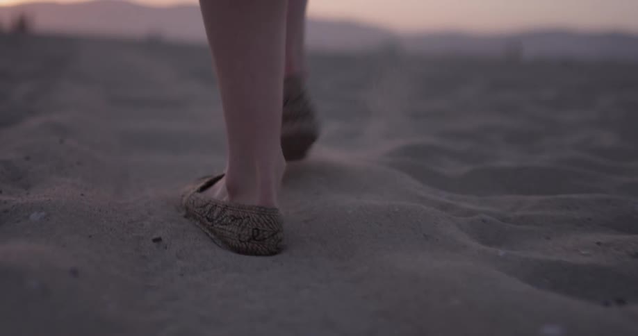 A woman walks through the sand during a beautiful sunset