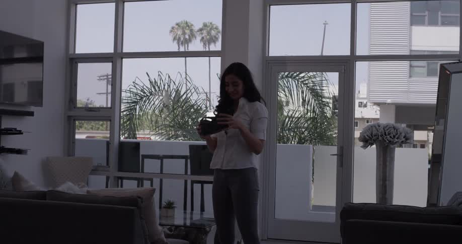 A woman stands in a bright house with a vr headset on until she takes it off