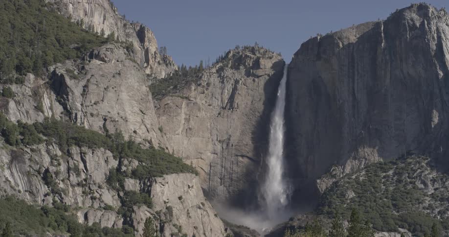 Water falls off the side of a mountain on a cloudless blue sky sunny day